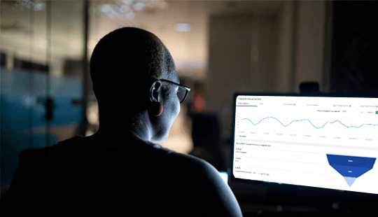 Person wearing glasses looking at analytics data on a computer screen in a dark office.