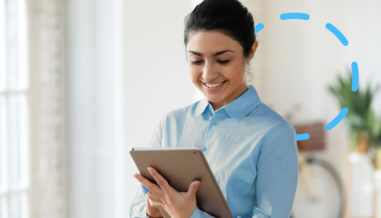 A person in a blue shirt is smiling while looking at a tablet in a well-lit room with a plant and a bicycle in the background, likely exploring mental health platforms.