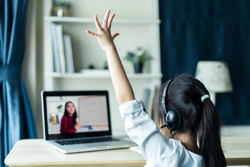 Young student raising her hand while using online teaching platforms for teachers