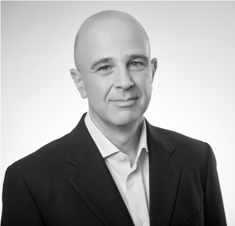 Black and white portrait of a bald man wearing a dark suit jacket and a light-colored shirt, looking directly at the camera with a neutral expression.