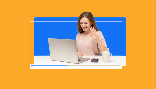 A woman sits at a table with a laptop, a smartphone, and a mug, waving and smiling at the screen. The background is a mix of blue and orange colors.