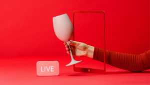 A hand holding a wine glass emerges from a tablet screen against a red background. A white "LIVE" sign is placed beside the tablet.
