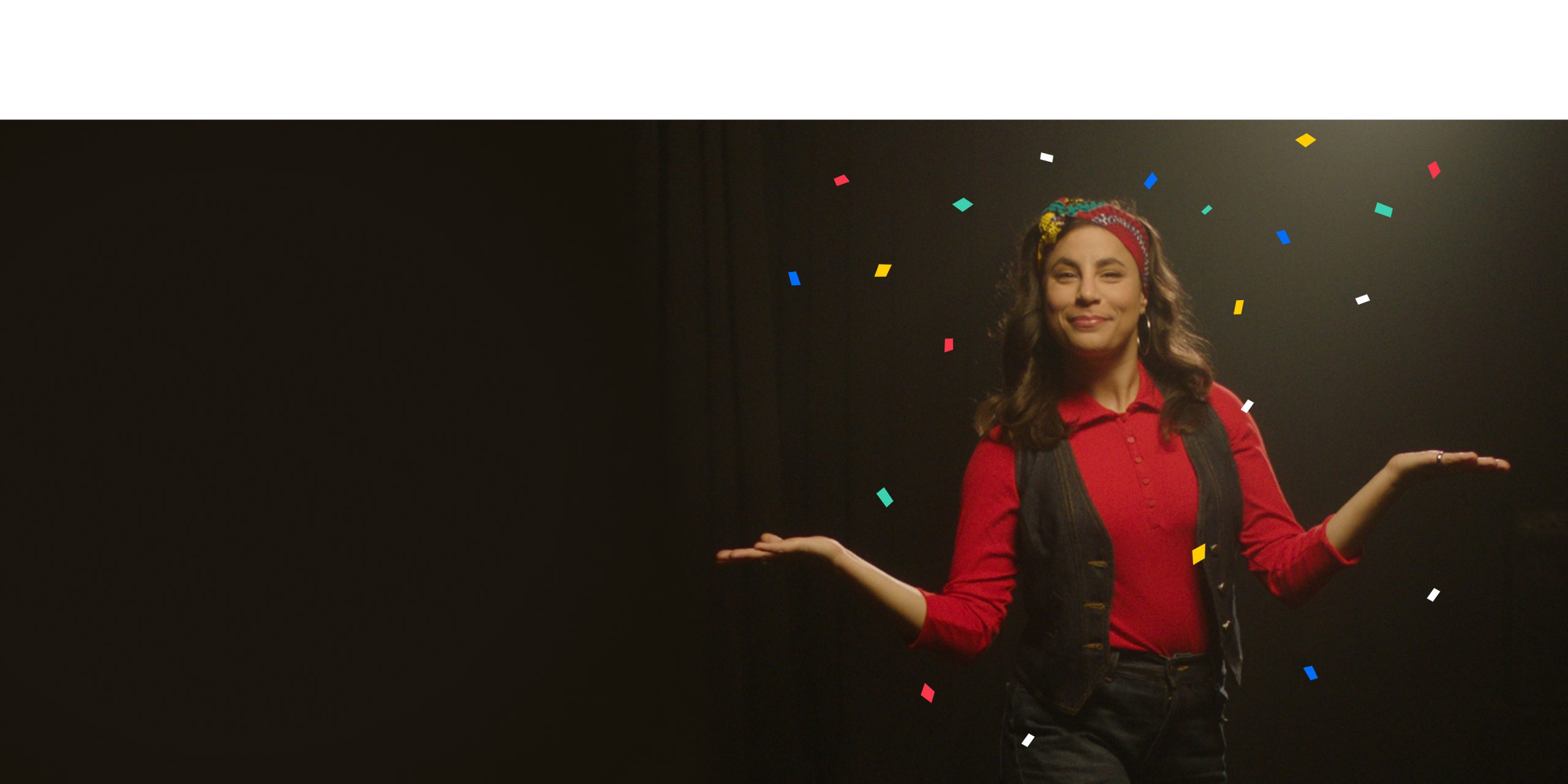 A woman in a red shirt, denim vest, and patterned headband, stands with her arms outstretched, surrounded by colorful confetti, against a dark background.