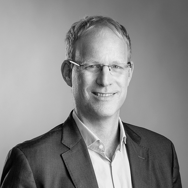 Man with glasses wearing a suit and smiling, posing against a plain background.
